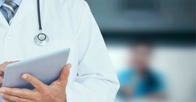 Composition of midsection of male doctor in lab coat using tablet over out of focus hospital