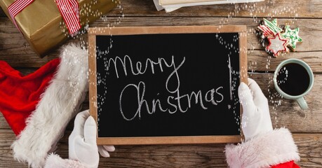 Composition of santa claus holding blackboard with merry christmas text and christmas presents