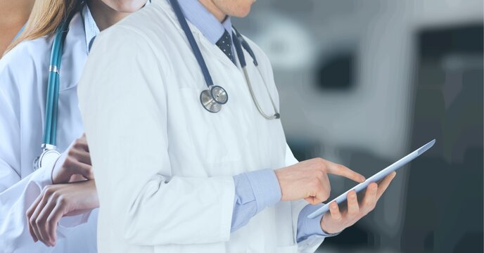 Mid section of male and female doctor using electronic devices against hospital in background