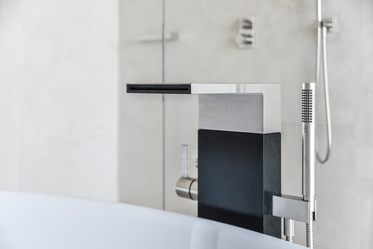 Minimalist Faucet Design With Wide Spout And Thin Shower Nozzle Above White Tub In Bathroom