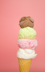 4 flavors of ice cream, coconut milk, strawberry, lime, and chocolate stacked in cones on pink background.