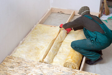 Caucasian Construction Worker with Roll of Insulating Material, Floor Insulating by Mineral Wool.
