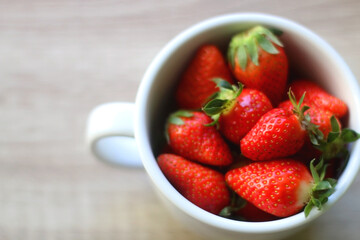 Mug filled with fresh strawberries on wooden table. Selective focus.