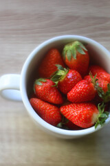 Mug filled with fresh strawberries on wooden table. Selective focus.