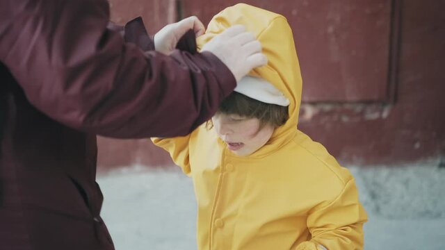 Mom puts on a little girl hood in a strong wind. The hurricane overtook the family suddenly and the child is confused. The concept of the elements and the storm