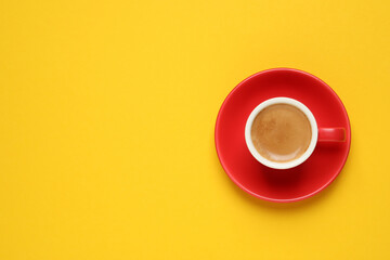 Aromatic coffee in red cup on yellow background, top view. Space for text