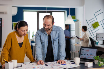 Project manager and assistant working together on charts for new business. Diverse team of business people analyzing company financial reports from computer.