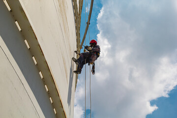Male worker rope access height safety inspection of thickness storage oil and gas tank