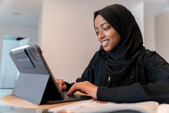 Black Muslim teenage girl doing work on a small electronic device 