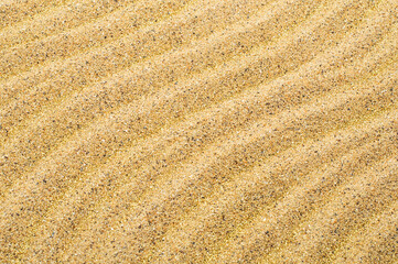 Summer background, sand with gold sparkles, drawing waves on the sand