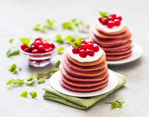 Pink pancakes with cream and fresh cranberries on a plate on a light gray background