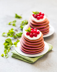 Vegan pink pancakes with fresh cranberries on a plate on a linen napkin on a light gray background