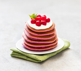 Berry pancakes with cream on a plate on a linen napkin on a light background