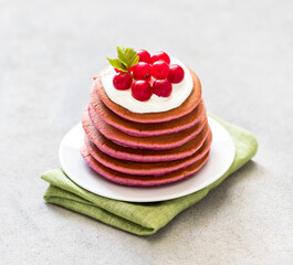 Vegan dessert, pink pancakes with cream and fresh cranberries on a plate on a light gray background