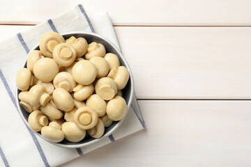 Delicious marinated mushrooms in bowl on white wooden table, top view. Space for text