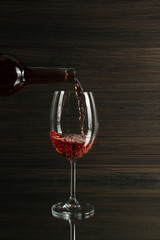 Pouring rose wine from bottle into glass on table against wooden background