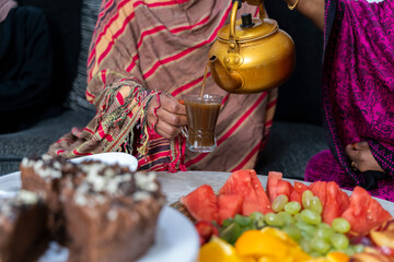 Black Muslim woman pouring coffee with desserts on table