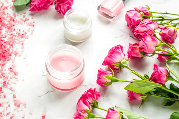 organic cosmetic with rose cream and petals on white background