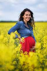Naklejka na ściany i meble Pregnant woman in a canola field