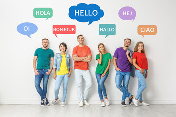 Happy people posing near light wall and illustration of speech bubbles with word Hello written in...