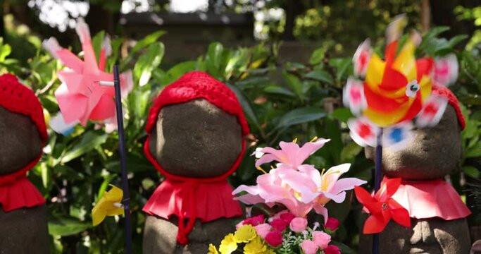 A slow motion of moving colorful windmills with Jizo statue daytime closeup