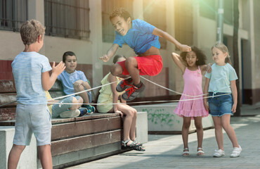 Smiling kids skipping on jumping elastic rope in european yard