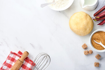 Ball of dough and ingredients flour, water, butter, sugar and rhubarb for baking on white marble background with dusting of flour. Recipe step by step. Selective focus. Top view.
