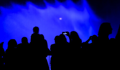 Fototapeta premium Silhouettes of people at the blue fountain at night.
