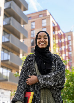 Black Muslim woman standing in park with a book in hand