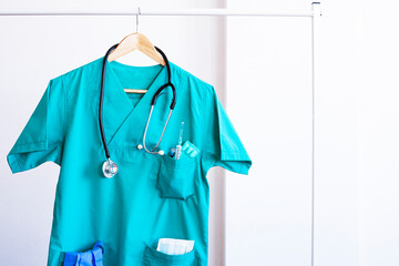 Closeup of a doctor's scrubs with stethoscope and lab coat on hangers.