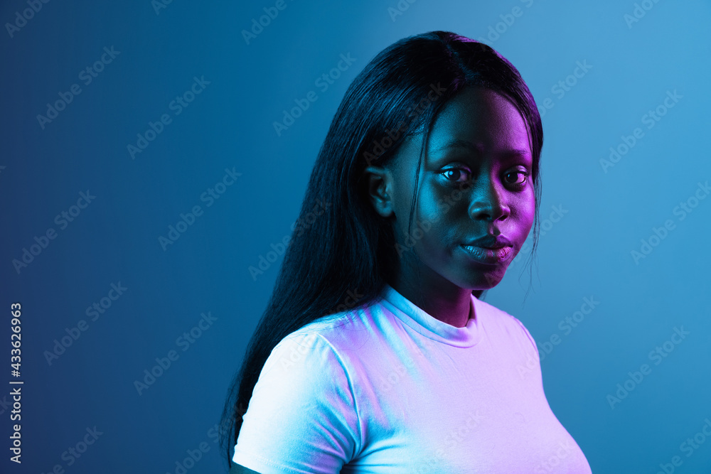 Wall mural One young African beautiful girl isolated over dark background in mixed neon light.