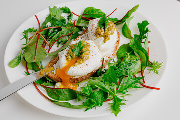 Avocado egg benedict with cream cheese Philadelphia. Poached eggs on healthy bread toast with hollandaise sauce. Cut egg. The yolk flows out. Green salad arugula leaves.