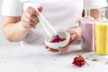 The girl grinds eucalyptus plants, dried rose flowers in a mortar with a pestle for home SPA body care. The concept of alternative medicine at home with a copy of the space.