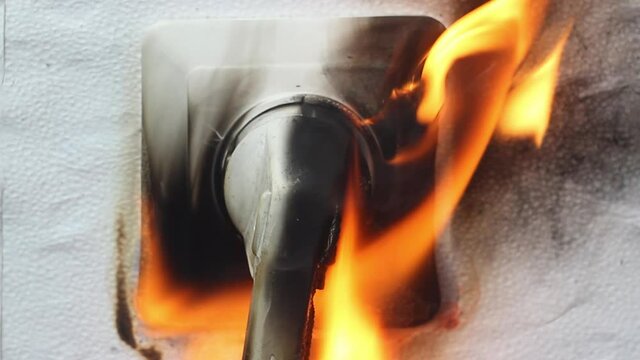 The plug from the electrical appliance inserted into the socket burns and melts from overvoltage. There was a short circuit of the wiring, and a fire started, charred wires, close-up,