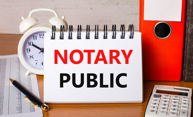 On the table are reports, a white alarm clock, a calculator, folders for papers, a pen and a white notebook with the text NOTARY PUBLIC. Business concept
