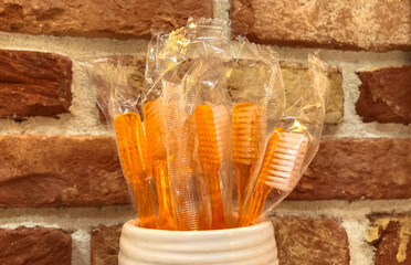 Disposable plastic orange toothbrushes in a ceramic cup against a red brick wall. Each toothbrush is individually wrapped. Dental supplies for oral care. Precautions against tooth decay. Dental health
