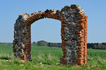 Remains of an old building masonry wall with arches in the middle of a green rape field under a...