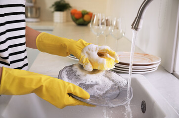 Woman washing plate above sink in kitchen, closeup