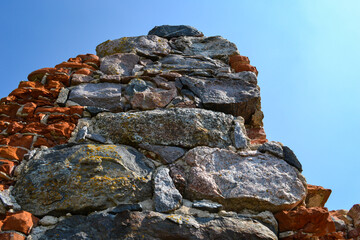 The ruins of the castle ruins with boulders and red bricks on the blue sky.