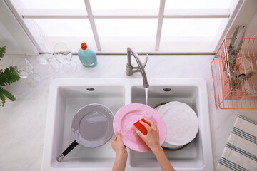 Woman washing plate above sink in kitchen, closeup