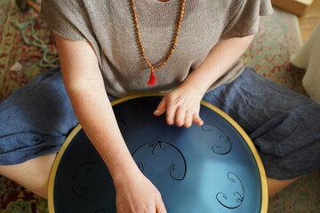 Obraz premium Woman with male bead around her neck is playing a RAV Drum, close up of womans hands playing hang drum, music instrument for sound healing.