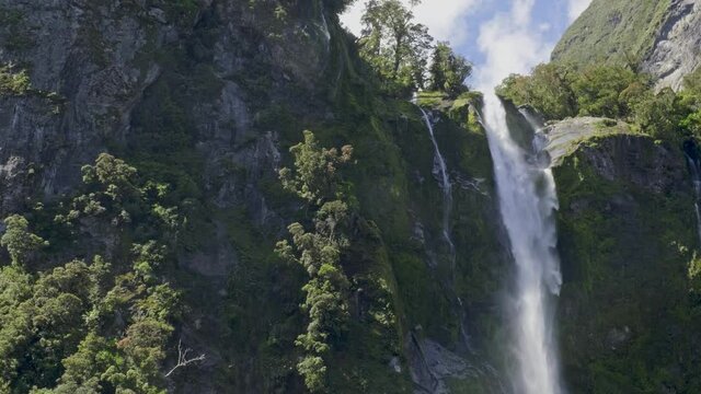Stirling Falls Flowing Over A Steep, Mossy Cliff At Milford Sound In New Zealand. - wide shot