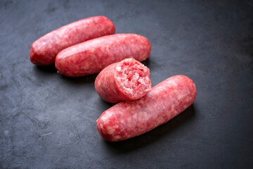 Traditional Italian raw salsiccia fresco meat sausage offered as close-up on a rustic black board