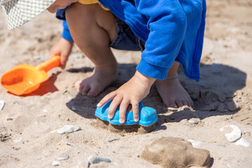 a child in a hat plays on the beach in the sand