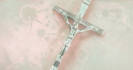 Composition of silver christian cross over covid 19 cells on pink background