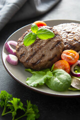 Cooked minced beef patty with vegetables. Dark background.
