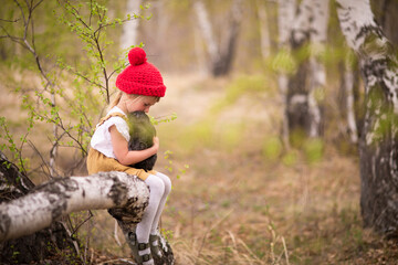 Little girl in a red hat in a spring forest plays with a rabbit in nature