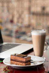 Girl eating piece of cake and cup of latte coffee in a cafe on the blur background of city