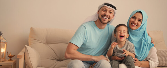 Happy Muslim family on sofa in living room, space for text. Banner design