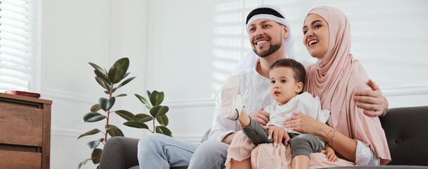 Happy Muslim family spending time together on sofa at home, space for text. Banner design